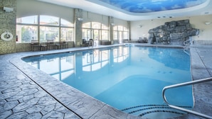 Une piscine intérieure dotée d’un sol en pierre, de grandes fenêtres et d’un mur en pierre décoratif.