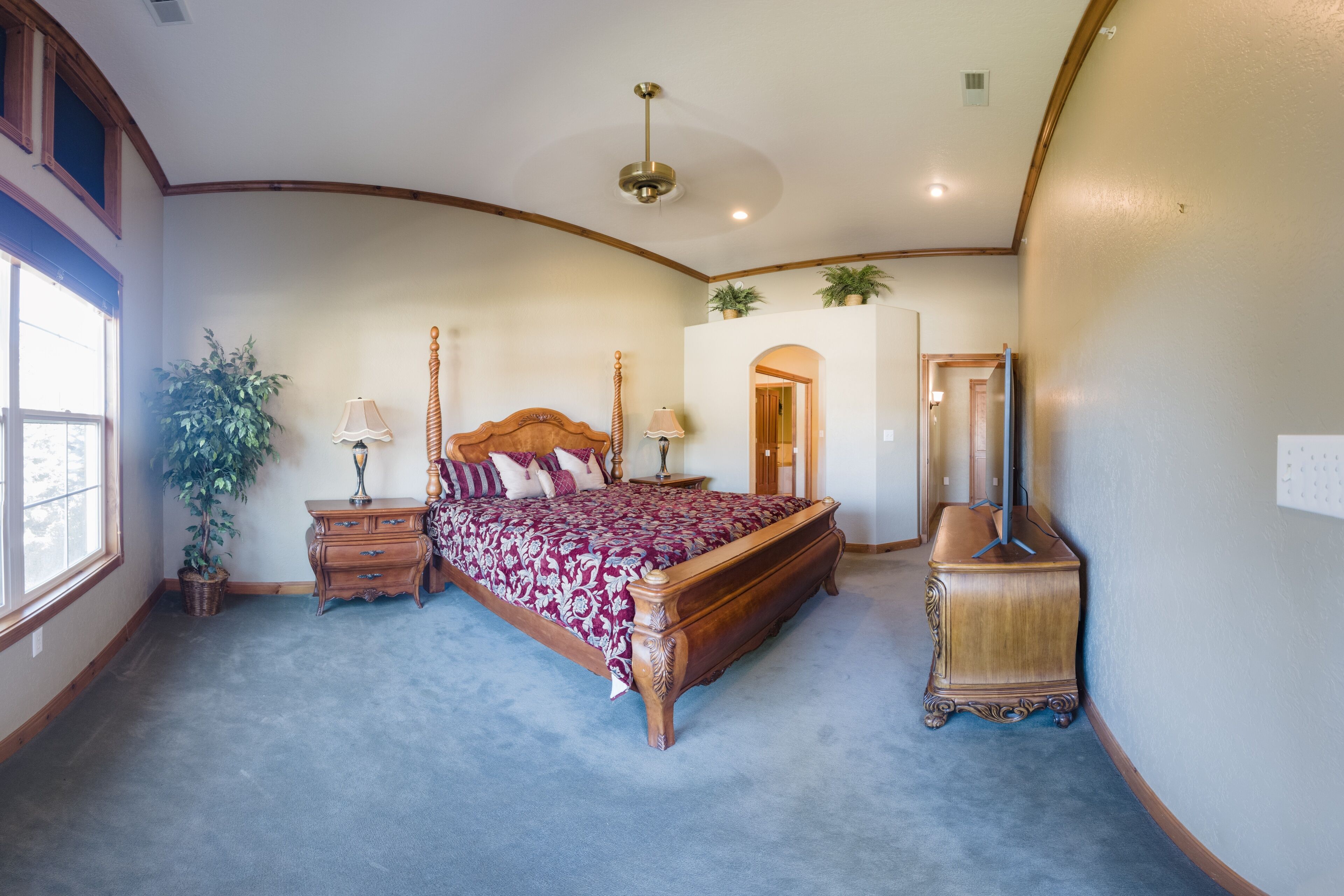 Quarto com uma cama grande, penteadeira, mesa de cabeceira, luminária, espelho e um vaso de planta.