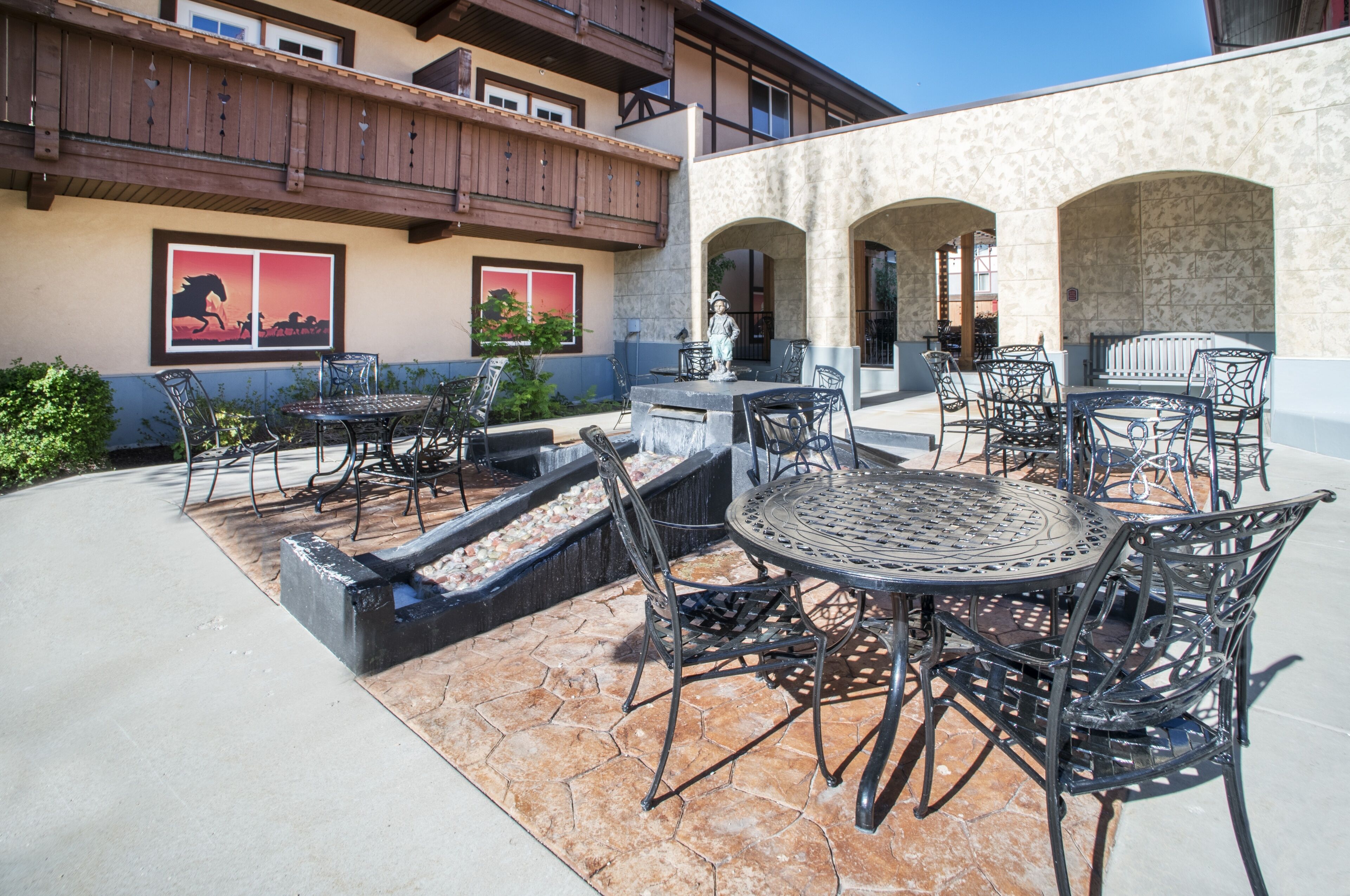 An outdoor patio area with multiple tables and chairs, a small water feature, and a mural on the building wall.