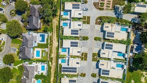 A residential area with multiple houses, each featuring a swimming pool and solar panels.
