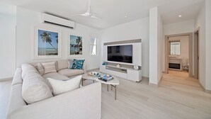 A modern living room with a sofa, coffee table, TV, and artwork. - Porters Place 11 3 Bedroom Home (Holetown)