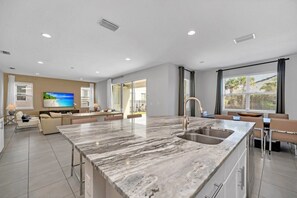 A modern kitchen with a large island, a dining area, and a living space with a TV. - Brand New Encore Resort 5 Bed Resort Home 5 Bedroom Villa (Kissimmee)