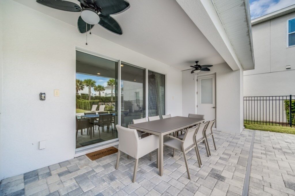 A patio with a table and chairs, a ceiling fan, and a sliding glass door leading to a garden.