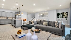 A modern living space with a kitchen, dining area, and a staircase leading to an upper level.