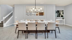 A dining area with a long table set for six, a chandelier, and a staircase to the left.