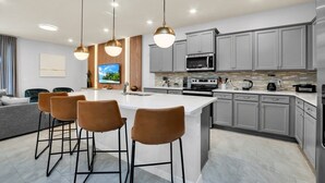 A modern kitchen with a central island, grey cabinets, stainless steel appliances, and pendant lighting.