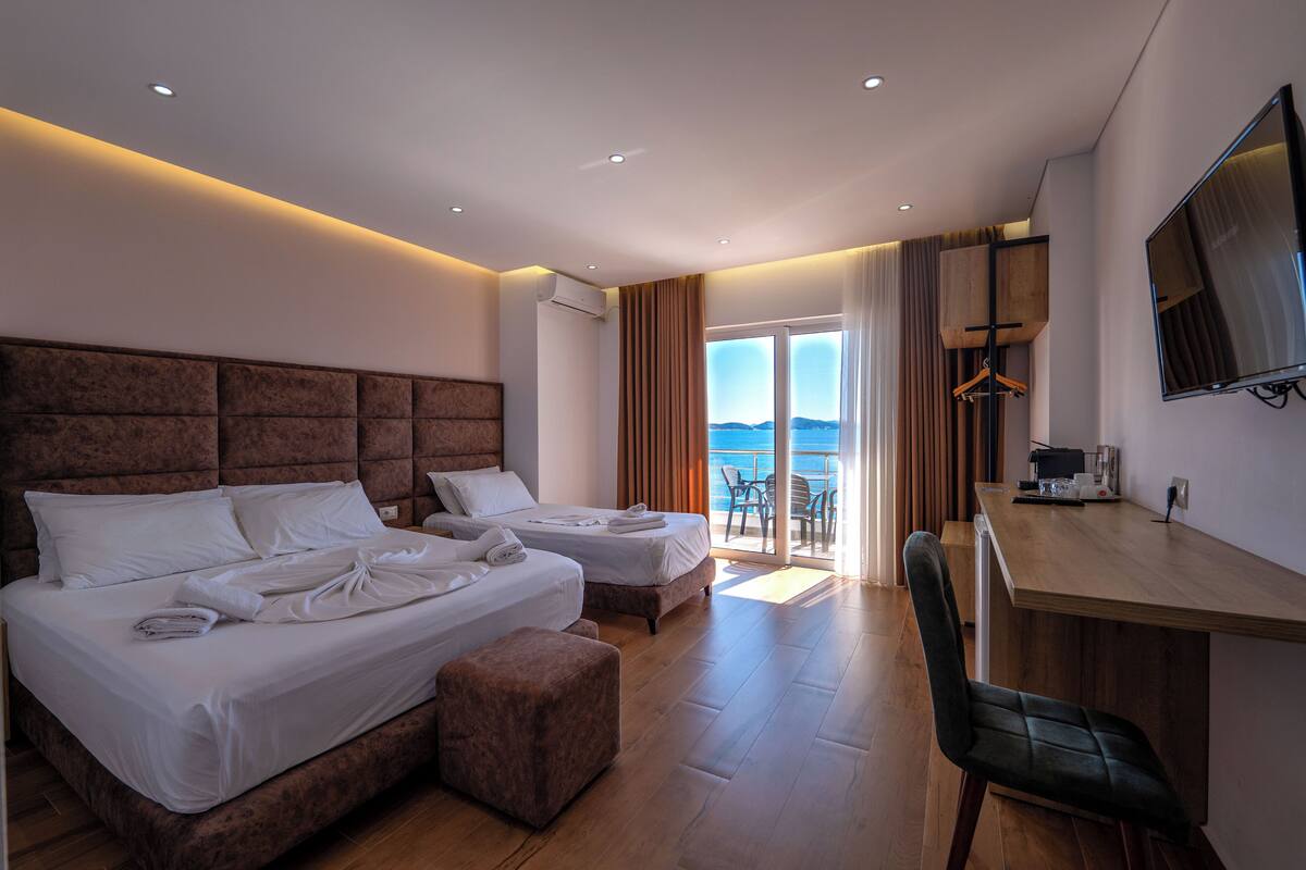 A hotel room with two beds, a desk, a chair, and a TV.