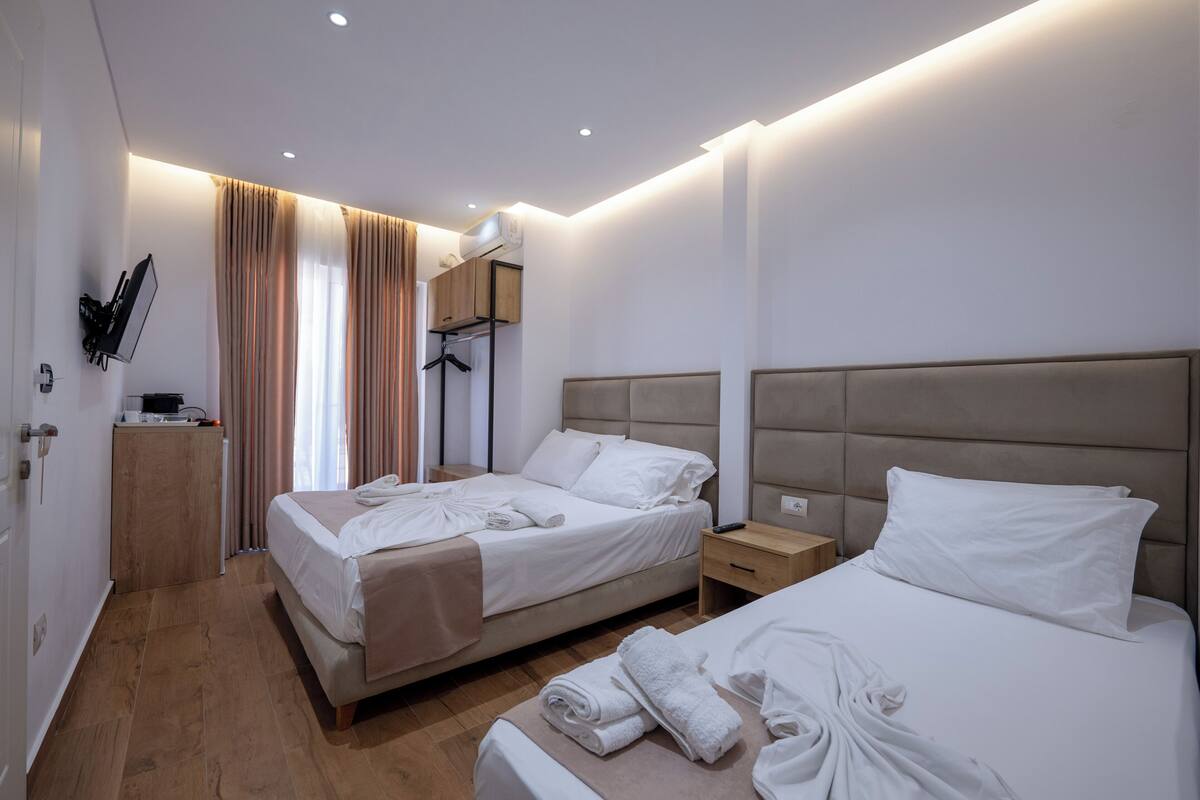 A hotel room with two beds, a wooden desk, a mirror, and a wardrobe.
