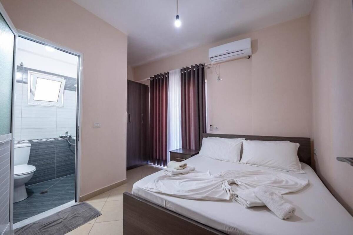 A hotel room with a bed, a bathroom with a toilet and shower, and an air conditioning unit on the wall.