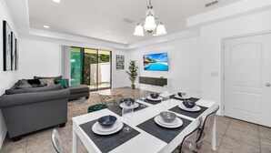 A modern living room with a dining table set for six, a grey sofa, and a TV mounted on the wall. - Tropical Escape 3 Bed Home In Beautiful Resort 3 Bedroom Condo (Davenport)
