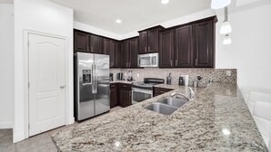A modern kitchen with dark wood cabinets, stainless steel appliances, granite countertops, and recessed ceiling lights. - Tropical Escape 3 Bed Home In Beautiful Resort 3 Bedroom Condo (Davenport)