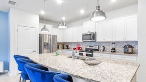 A modern kitchen with white cabinets, a granite countertop, stainless steel appliances, and blue bar stools. - Ultimate 5 Bedroom Windsor Island Resort 3966Lana 5 Villa (Davenport)