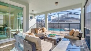 A spacious balcony with wicker furniture, a glass table, and a view of a swimming pool and neighboring buildings. - Florida Garden Luxury Home With Private Pool & Spa 6 Bedroom Villa (Kissimmee)