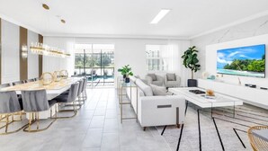 Una sala de estar moderna y bien iluminada, con comedor, sofá, mesa de centro y televisor en la pared.