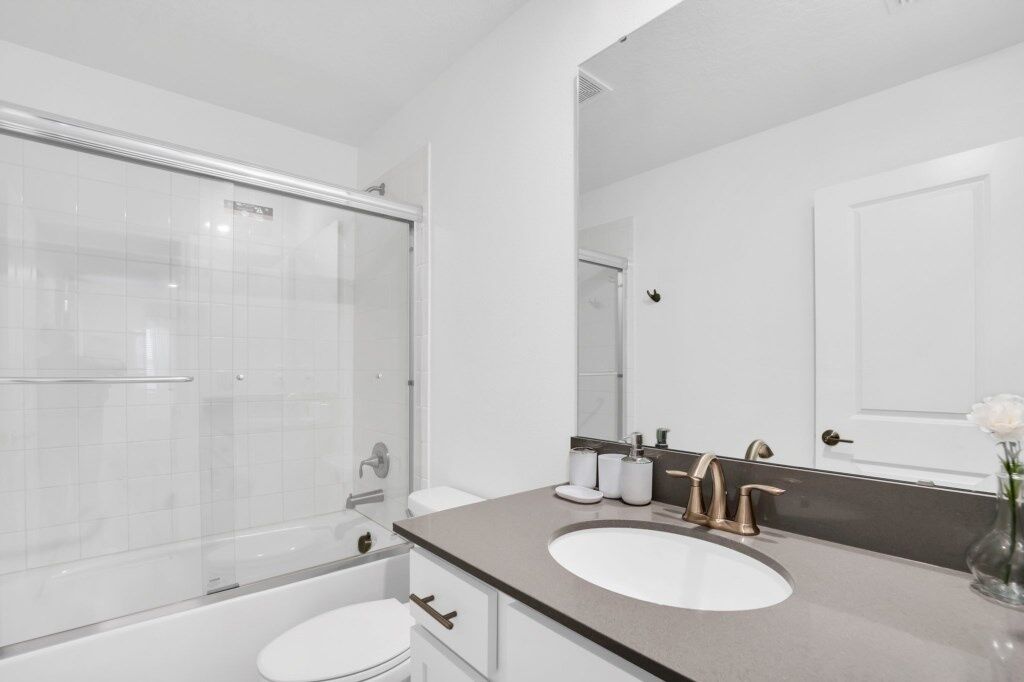 Un bagno moderno con box doccia in vetro, un water bianco, un lavabo con mobile contenitore e uno specchio.