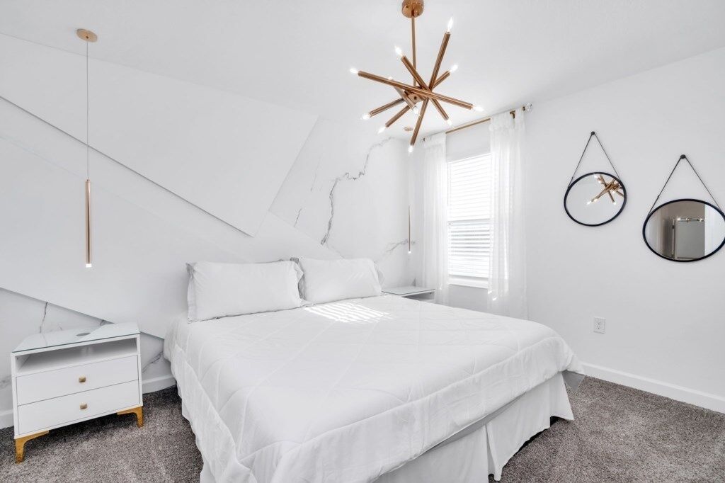 Une chambre à coucher avec un lit, une table de chevet, un luminaire suspendu et une fenêtre avec des stores.