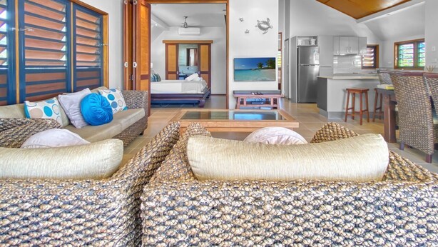 A modern living room with a sofa, a bed, a TV, and a kitchen area. - Pure Magnetic Villa 10 (Nelly Bay)
