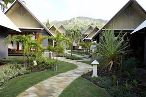 A resort with multiple bungalow-style buildings, a central pathway, and a mountainous backdrop.