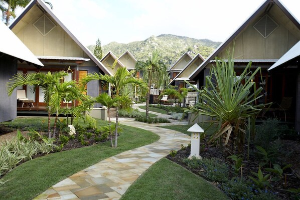 A resort with multiple bungalow-style buildings, a central pathway, and a mountainous backdrop.