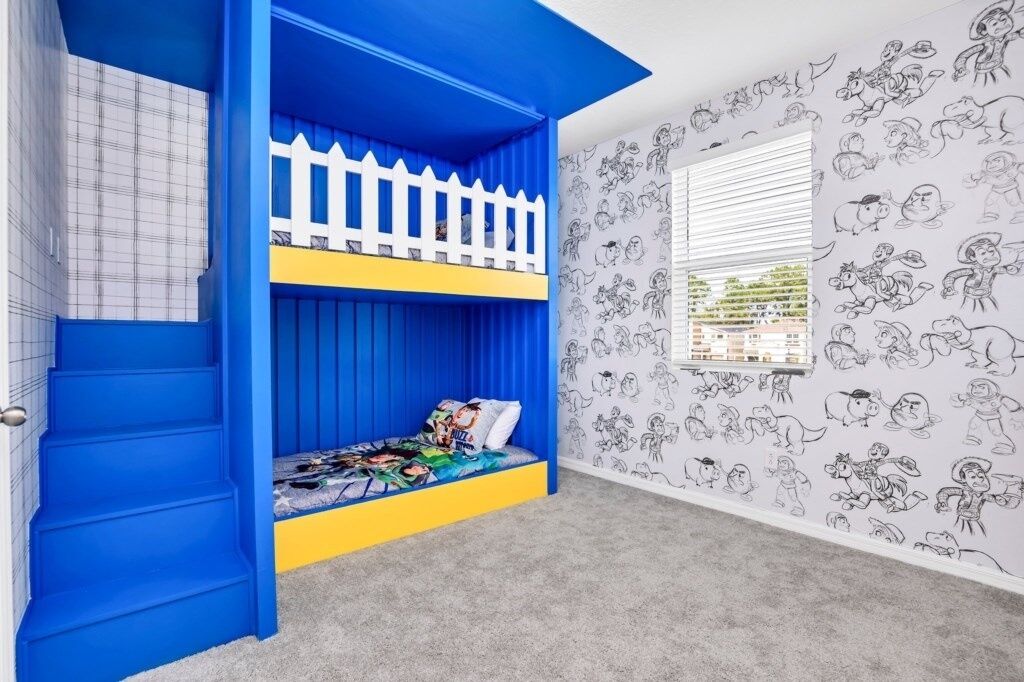 A child's bunk bed with blue and yellow accents, a white picket fence, and cartoon-themed wallpaper.