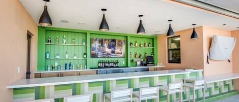 A bar area with a green backdrop, multiple liquor bottles, and bar stools.