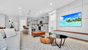 A modern living room with a sofa, coffee table, and a dining area with chairs. - 3516laven 8 Bedroom Villa (Davenport)