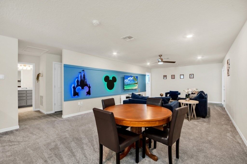 A modern dining room with a round wooden table and chairs, a blue accent wall with framed pictures, and a ceiling fan.