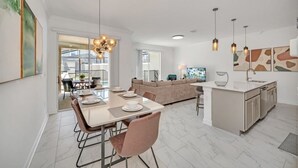 A modern kitchen with a central island, a dining area with a table and chairs, and a living area with a sofa. - 4228para 4 Bedroom Townhouse (Kissimmee)