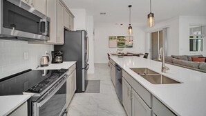 A modern kitchen with stainless steel appliances, a white countertop, and a central island with a sink. - 4228para 4 Bedroom Townhouse (Kissimmee)