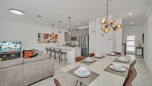 A modern living room with a sofa, dining table, and chairs. There is a kitchen area with cabinets and appliances. - 4228para 4 Bedroom Townhouse (Kissimmee)