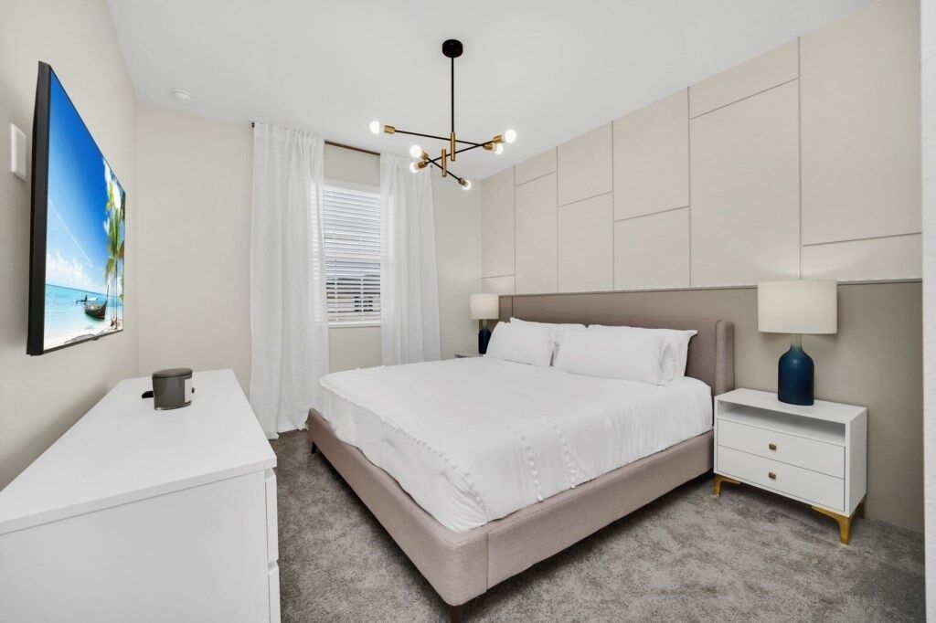 A bedroom with a bed, bedside tables, a desk, a TV, and a window with curtains.