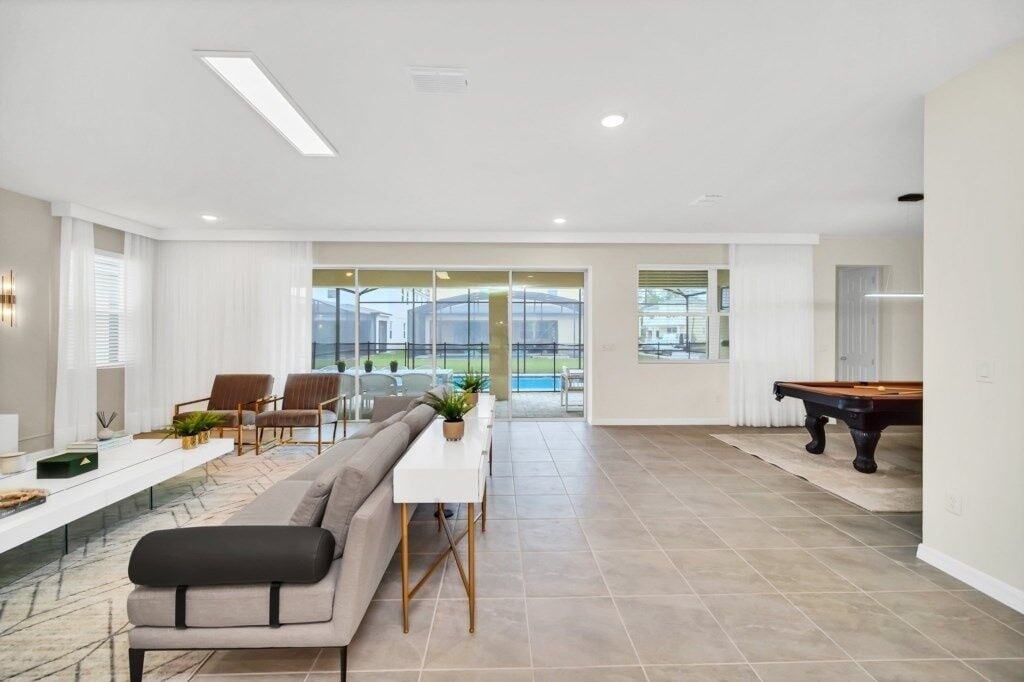 A modern living room with a sofa, dining table, chairs, and a pool table.