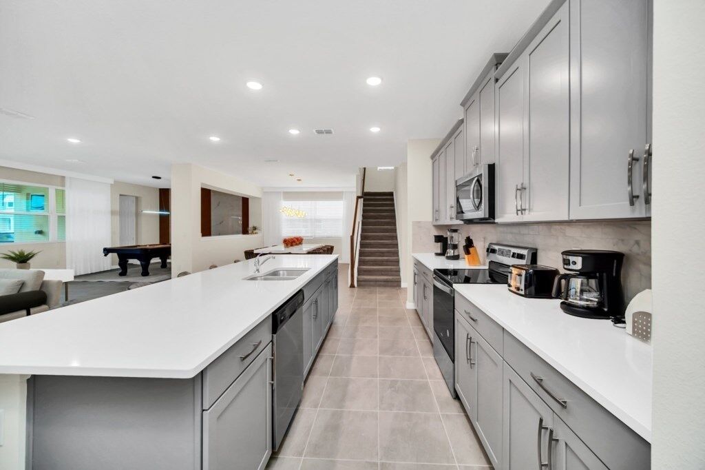 A modern kitchen with a central island, grey cabinets, and a staircase leading to another level.