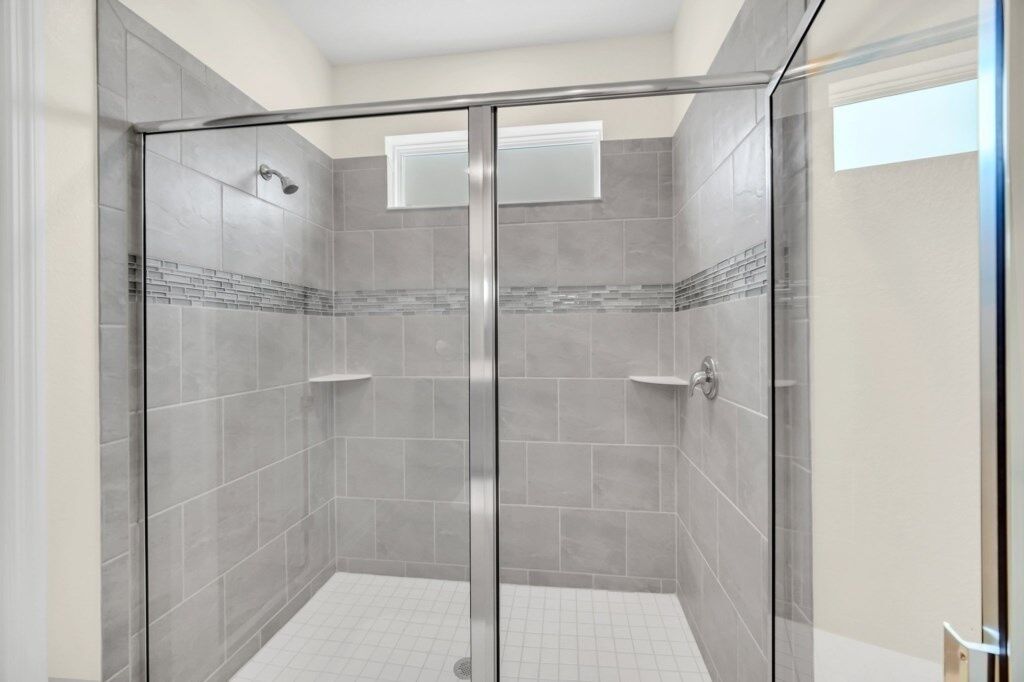 A glass-enclosed shower with grey tiles and a small window.