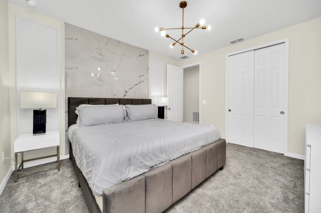 A bedroom with a large bed, a marble wall, a chandelier, and white doors.