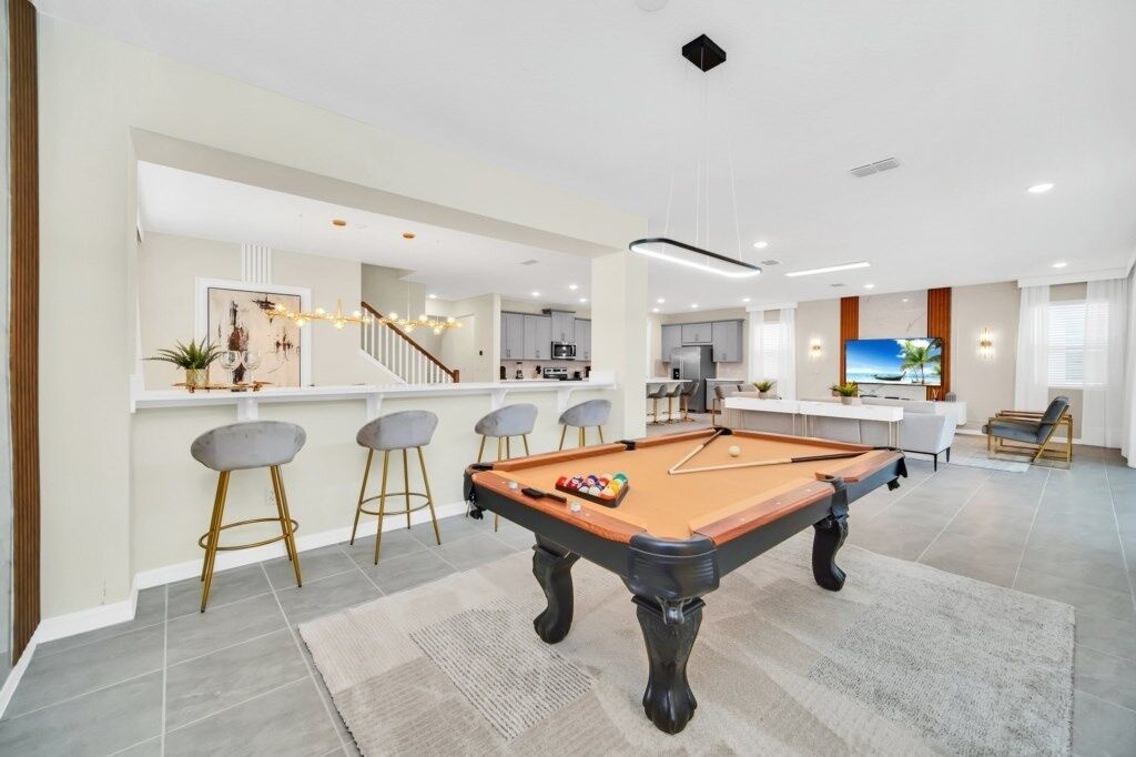 A modern living room with a pool table, bar area, and kitchen in the background.
