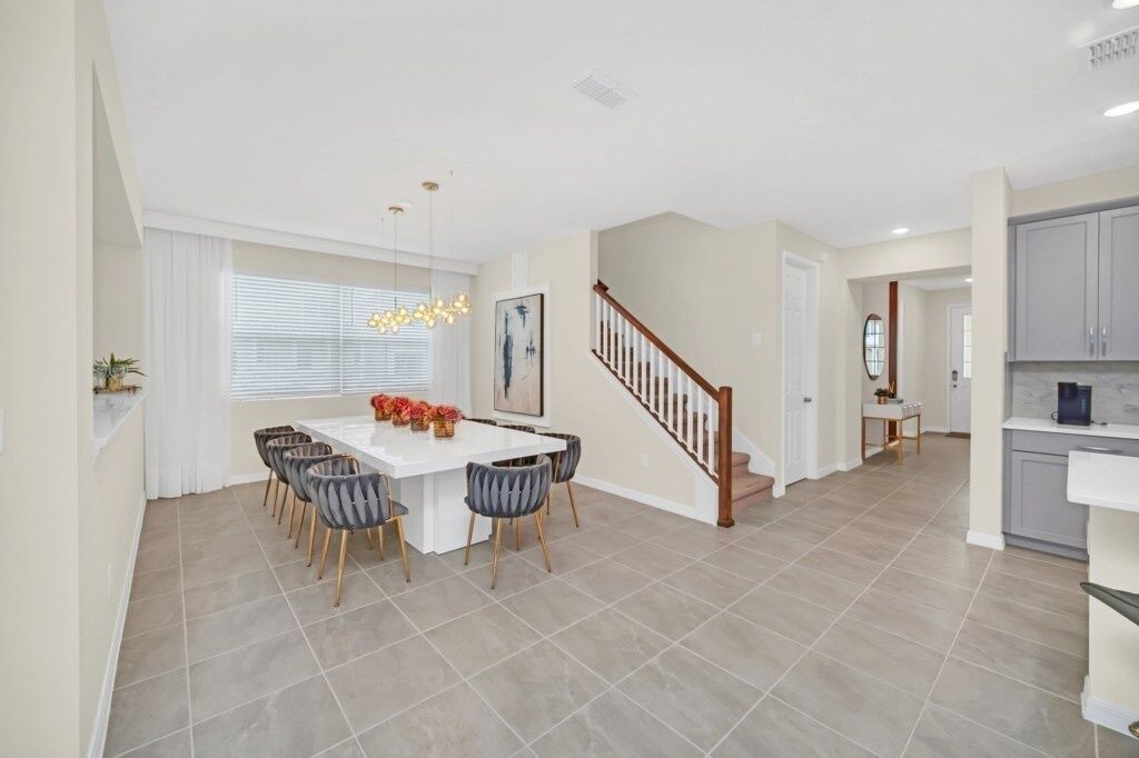 A spacious dining area with a white table and chairs, a staircase, and a kitchen area.