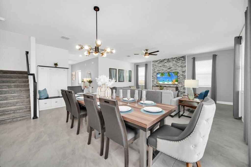 A modern dining area with a wooden table, grey upholstered chairs, and a chandelier.