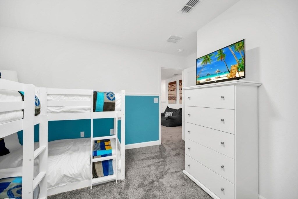 Quarto de criança com beliche, televisão e cómoda branca.