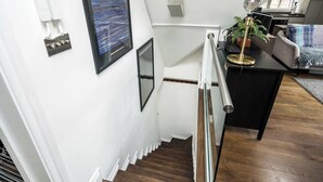 Una escalera de madera con barandilla metálica, que conduce a un rellano con un escritorio y una planta en maceta.