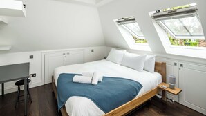 Un dormitorio con cama, escritorio y dos tragaluces.