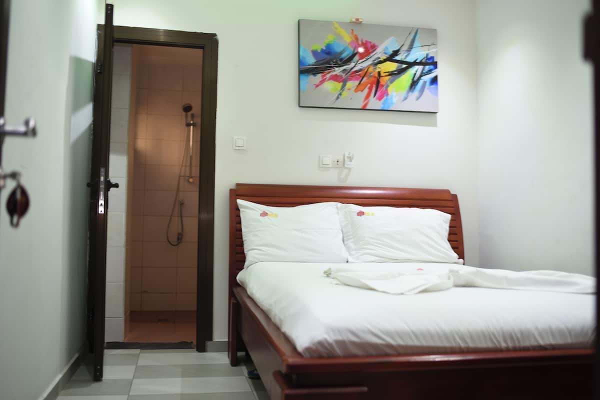 A hotel room with a wooden bed, white bedding, a shower, and a colorful abstract painting on the wall.
