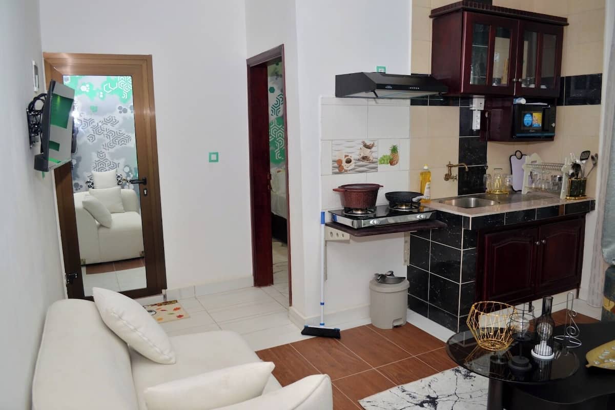 A compact living space with a kitchenette, a sofa, a dining table, and a mirror reflecting a room with a bed.