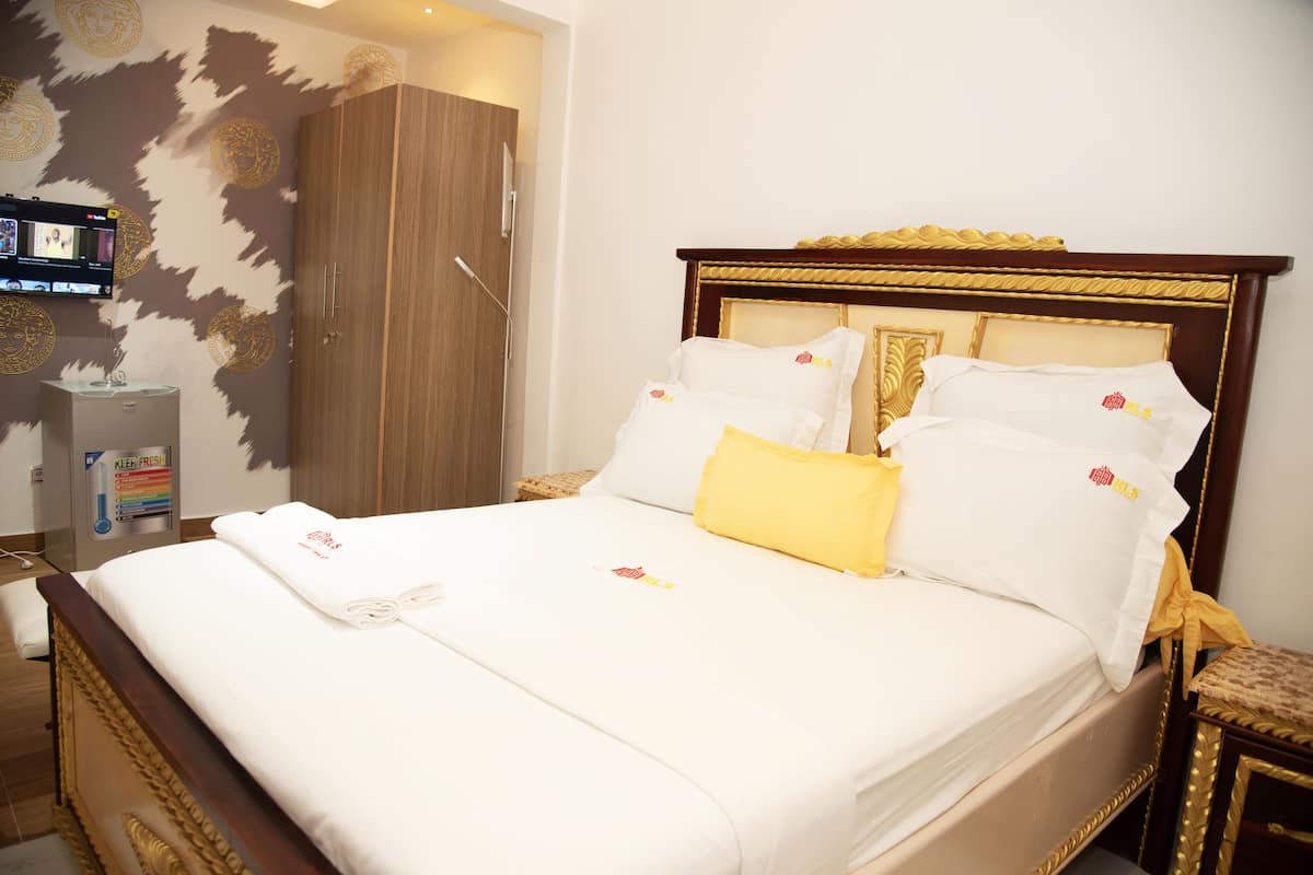 A neatly made bed with white linens and a yellow accent pillow, a wooden wardrobe, and a television mounted on the wall.