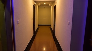 A narrow, well-lit hallway with a polished floor, flanked by plain walls and doors, leading to a room with a visible door at the end. - ANANYA COMFORTSS-OPP RAHEJA RESIDENCY  (Bengaluru)