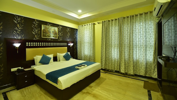 A hotel room with a large bed, a nightstand, a wall-mounted lamp, and a painting. - ANANYA COMFORTSS-OPP RAHEJA RESIDENCY  (Bengaluru)