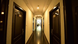 A long, narrow hotel corridor with dark wooden doors on either side, leading to a bright, well-lit room at the end. - ANANYA COMFORTSS-OPP RAHEJA RESIDENCY  (Bengaluru)