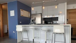 Eine moderne Küche mit weißen Schränken, einer zentralen Kochinsel mit Barhocker und Pendelleuchten.