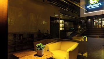 Een modern interieur met een gele bank, een houten tafel met een plant en een neonbord voor Hessnerly.