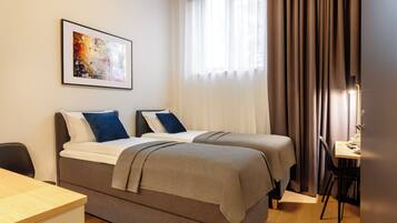 Quarto de hotel com duas camas, uma escrivaninha e uma cadeira.